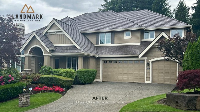 A two story suburban house with fresh gray roofing, tan siding, white trim, and a well maintained yard featuring green bushes, trees, and red flowers. Landmark Roofing and Siding logo is in the corner.