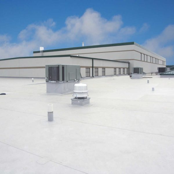 A flat, white commercial rooftop with multiple HVAC units and pipes. The sky is clear with a few clouds, and a large, rectangular building with green accents is in the background.